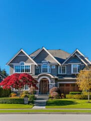 A classic luxurious two-story house with striking red autumn leaves on the tree in the front lawn showcasing seasonal beauty