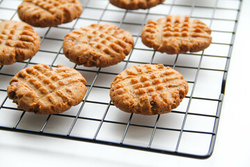 Process of making peanut butter cookies.  Peanut butter cookies are cooling after baking on a rack on a white background.