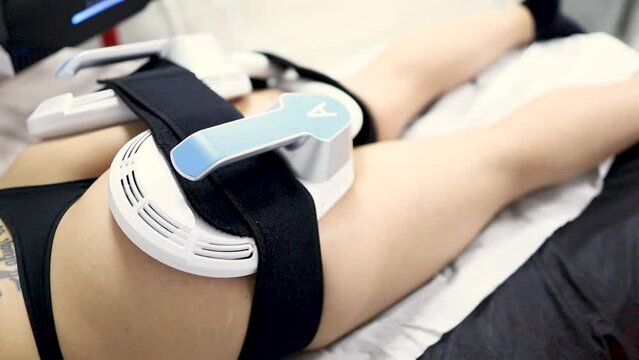 An unrecognizable young woman undergoes a treatment that uses high-intensity electromagnetic energy to firm muscles and reduce fat. The woman has the device on her buttocks to strengthen them.