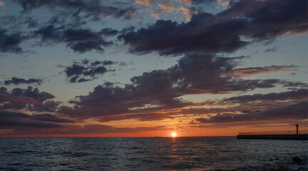 Panoramic view: seascape, setting sun over water surface on cloudy sky