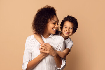 A smiling African American woman and her cheerful young son share a tender embrace, both sporting...