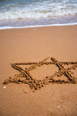 A young attractive student is relaxing by the seashore and drawing a star of David.