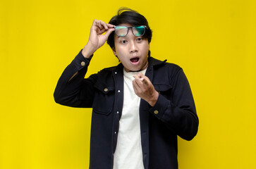 wow expression of asian man with glasses pointing finger to copy space showing something good. 