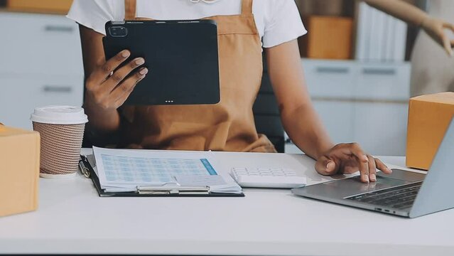 Young Asia lady fashion designer using mobile phone receiving purchase order and showing clothes recording video live streaming online at shop. Small business owner, online market delivery concept.