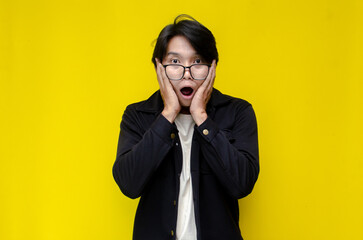 Ecstatic asian man touching face and lowering his glasses as a shocked and surprissed exppression. 