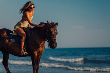 Side view of a woman riding a horse on a beach during a sunset