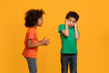 African American young girl appears to be talking animatedly to a boy, who is covering his ears with his hands, possibly indicating he is not interested in hearing what she has to say.