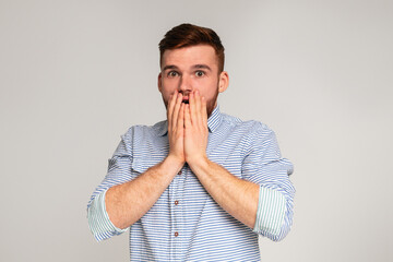 Surprised guy. Shocked man holding his hends hiding open mouth on studio background, panorama, copy...