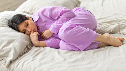 Depressed young middle eastern woman is curled up in a comfortable position, wearing soft purple...