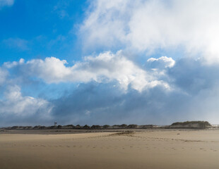 Blue sky and approaching rain clouds over an empty sandy beach on the ocean shore.