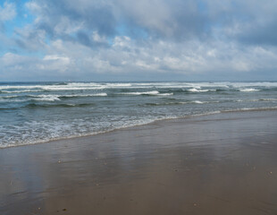 The waves of the Atlantic Ocean wash the sandy beach, the horizon is visible, the day is overcast.	