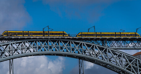 Two yellow trains on an iron bridge; bottom view against blue sky.