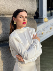 beautiful woman with dark hair in luxurious white silk dress and accessories posing by the Alexandre III bridge in Paris