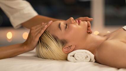 The photo shows a blonde woman lying down during a facial massage at a spa, with a calm and peaceful expression, enhancing her youthful glow