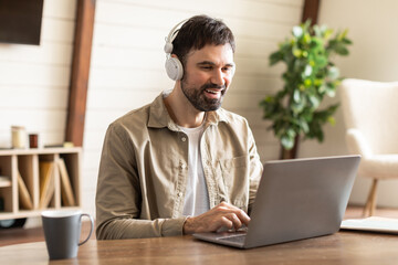 A man is seated at a table with a laptop open in front of him. He is wearing headphones and appears...