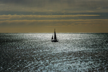 Backlit image of a sailboat sailing in the Atlantic Ocean, with a beautiful sky as a background and the sea with its shiny surface.