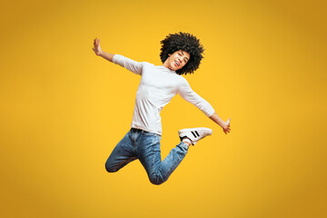 Modern hip-hop style black curly man jumping in air, dancing on orange background