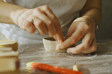 A woman makes holes using a tool in a clay craft - a candlestick.