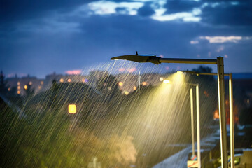 Krople deszczu w świetle ulicznej lampy na osiedlu w mieście. 
