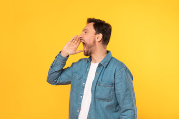 A man is standing in front of a vibrant yellow wall with his mouth open in a surprised expression....
