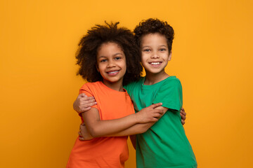 Two young African American children, a boy and a girl, are embracing each other in a warm hug. They...
