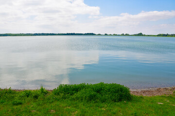 A vast lake with a lush green bank under a cloudy sky