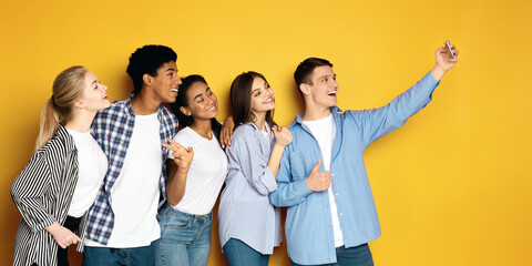 A diverse group of five multiethnic teenagers is gathered closely together, posing for a selfie....