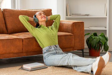 A woman is lying on the floor, headphones on, listening to music. She appears relaxed and engrossed...