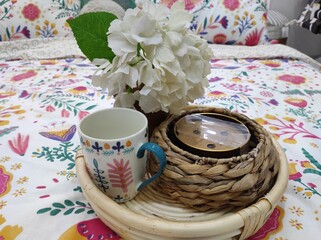 Salver with cup, flower and candle on bed, home decoration