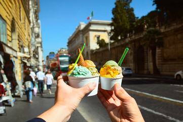 Couple with  bright  sweet Italian ice cream gelato with different flavors  in the hands  on the square in Rome, Italy