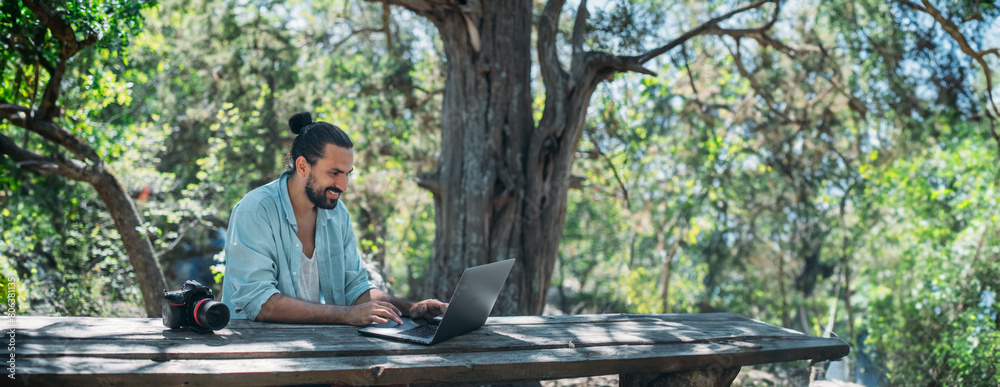 Wall mural Male photographer working on a laptop outdoors in a camping