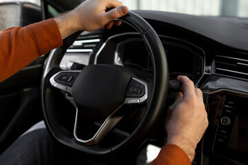 Over the shoulder view of man sitting in car on driver's seat, turning on windshield wipers, holding hands on steering wheel