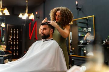 Expert barber meticulously trims and styles a man's hair using scissors, focusing on precision and...