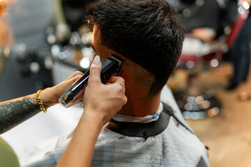 Close-up view of a female barber's hands expertly using clippers to perfect a male client's haircut, focusing on detail and craftsmanship in a stylish barber shop - obrazy, fototapety, plakaty