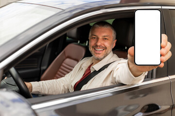 Cheerful middle aged man showing cellphone with blank screen through opened car window, driver...