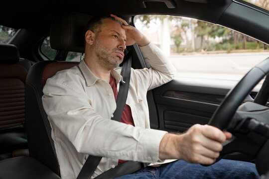 Thoughtful tired man driving car, stuck in traffic, pensive male driver with fasten seat belt looking at road, leaning on his hand