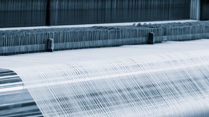 A machine is weaving a fabric with many different colored threads. The machine is blue and white