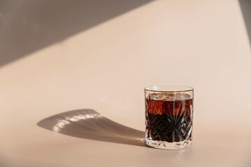 Whiskey cola cocktail with strong alcohol and ice in highball glass on light beige background with...