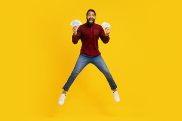 Indian man wearing a red sweater and blue jeans exuberates happiness while jumping in the air. He...