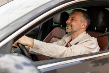 Cheerful middle aged man driving car, shot from outside. Happy male in casual outfit riding his...