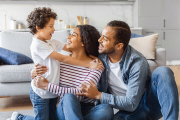Fototapeta premium African American man, woman, and child are seated on the floor in front of a couch. They appear to be engaged in conversation or possibly watching something together.