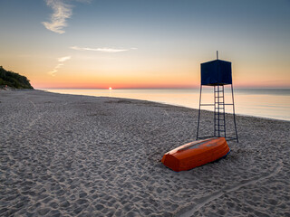 Sunset at beach with lifeguard hut and boat by Sea