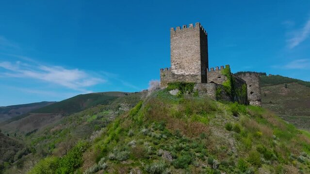 Low angle orbiting drone shot of Doiras Castle on a hill In Cervantes, Lugo, Spain on a sunny day