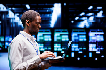 African american system administrator typing supercomputer hub contingency plan on laptop to...