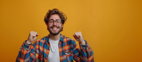 Cheerful young Caucasian man celebrating an achievement, yellow background, shirt, glasses, T-shirt.