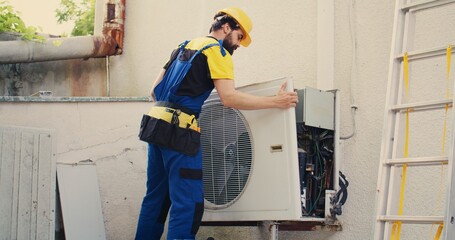 Precise serviceman starting work on malfunctioning outdoor air conditioner, dismantling condenser...