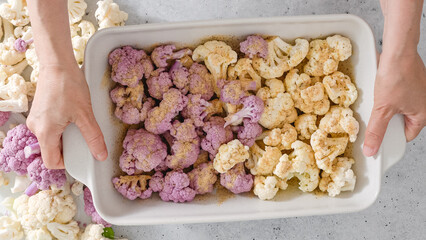 Cauliflower, white and purple, in baking pan with garlic seasoning, ready to be baked, woman hands