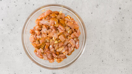 Glass bowl with the chopped marinated chicken meat mixture inside, flat lay