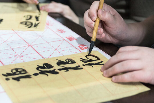Chinese Calligraphy. Female hand with Asian hieroglyphs, brush and on wooden background, closeup.