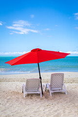 Two empty beach chairs and an umbrella on a beautiful day in the Caribbean
